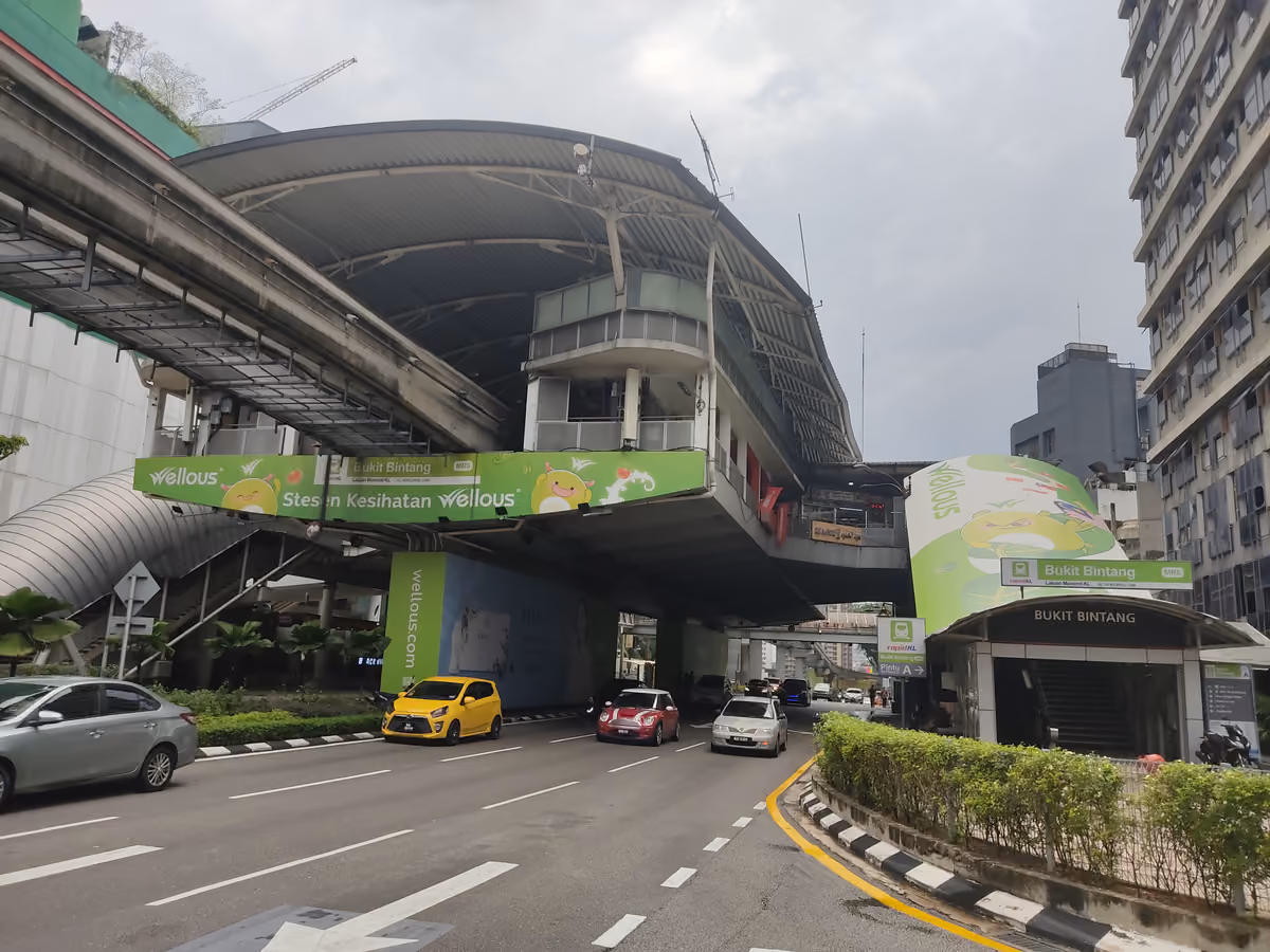 An elevated monorail station with a curved roof above a wide street, with a green Bukit Bintang sign on the station and on a street-level entrance