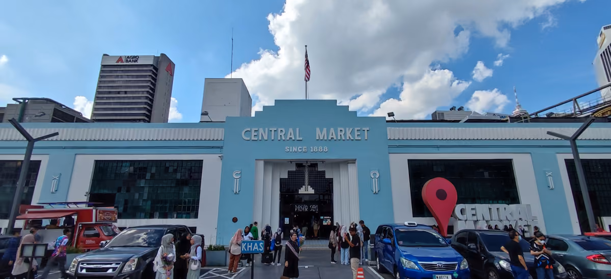 The pale blue Art Deco front of Central Market, its name over the entrance, with parked cars and visitors in front and office towers behind