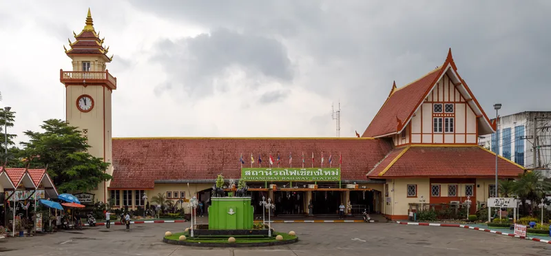Chiang Mai railway station: a long building with a red-tiled roof, a clock tower on the left and a green sign reading Chiangmai Railway Station