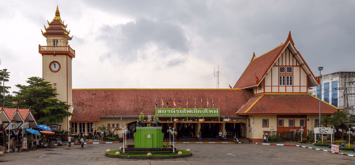 Chiang Mai railway station: a long building with a red-tiled roof, a clock tower on the left and a green sign reading Chiangmai Railway Station