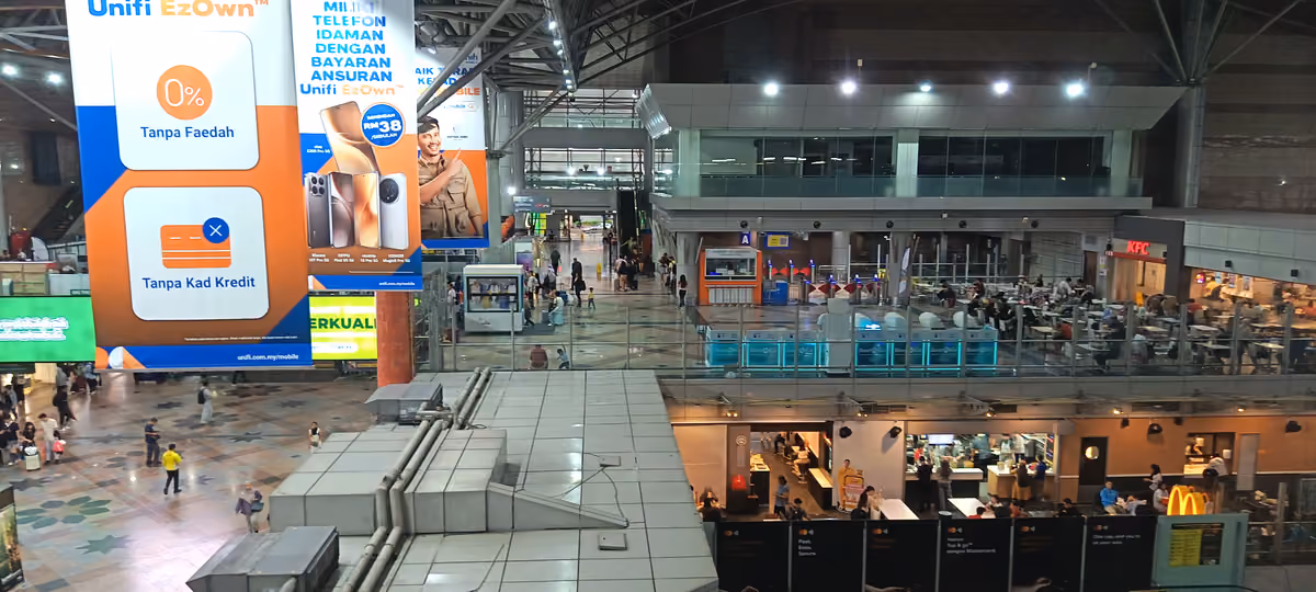 The large, high-roofed concourse of a rail station seen from above, with ticket machines, shops and travellers crossing a tiled floor