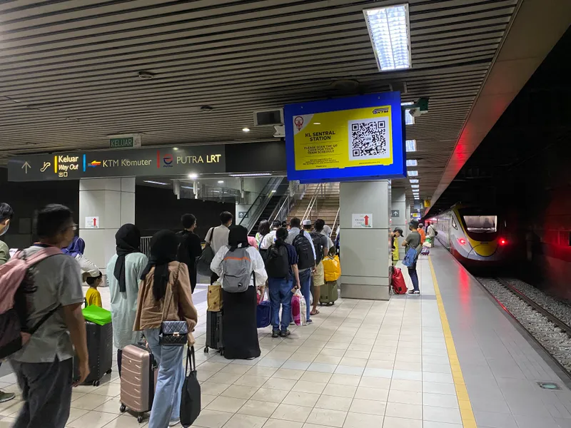 Passengers with suitcases queue on an underground platform at KL Sentral beside an ETS train, under a yellow KTMB sign reading KL Sentral Station