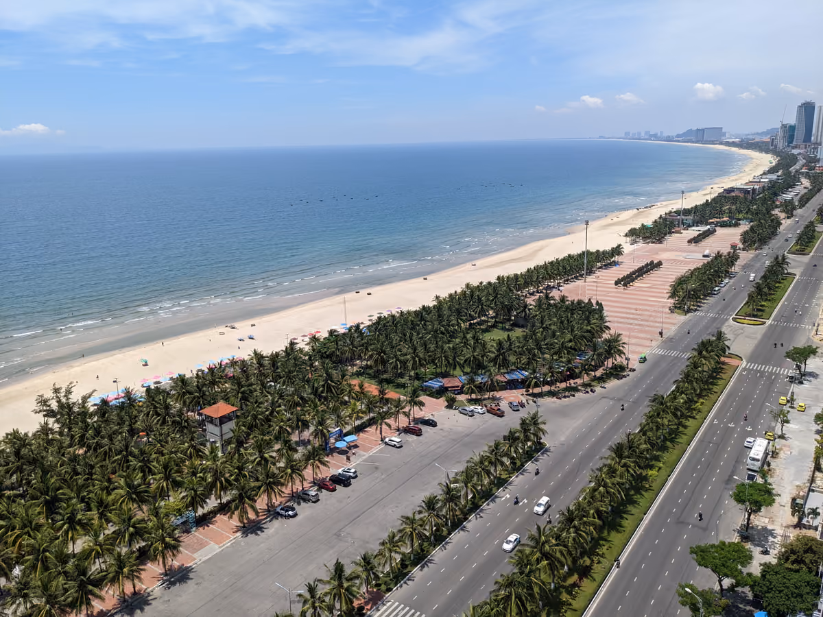 My Khe beach from above: pale sand, a line of palm trees, a seafront road and tall buildings along the curving coast