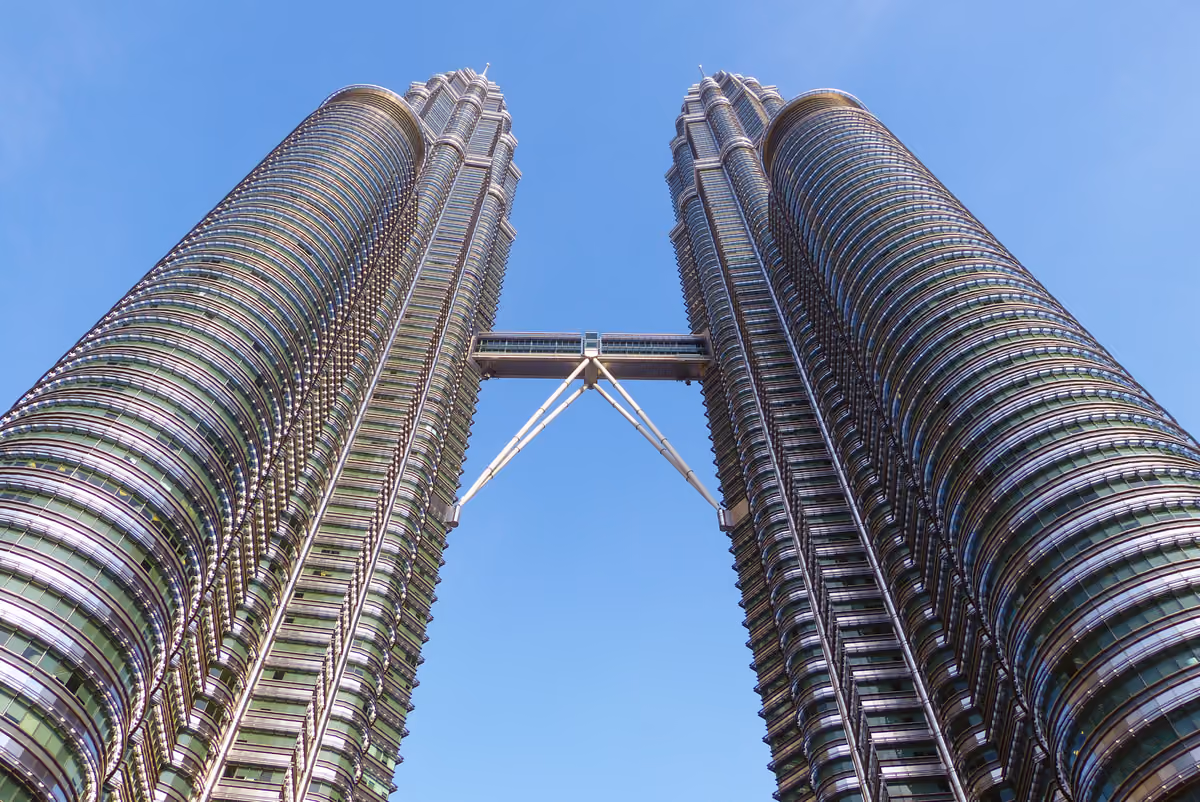 The two Petronas towers seen from below against a blue sky, joined halfway up by the Skybridge and its angled supports