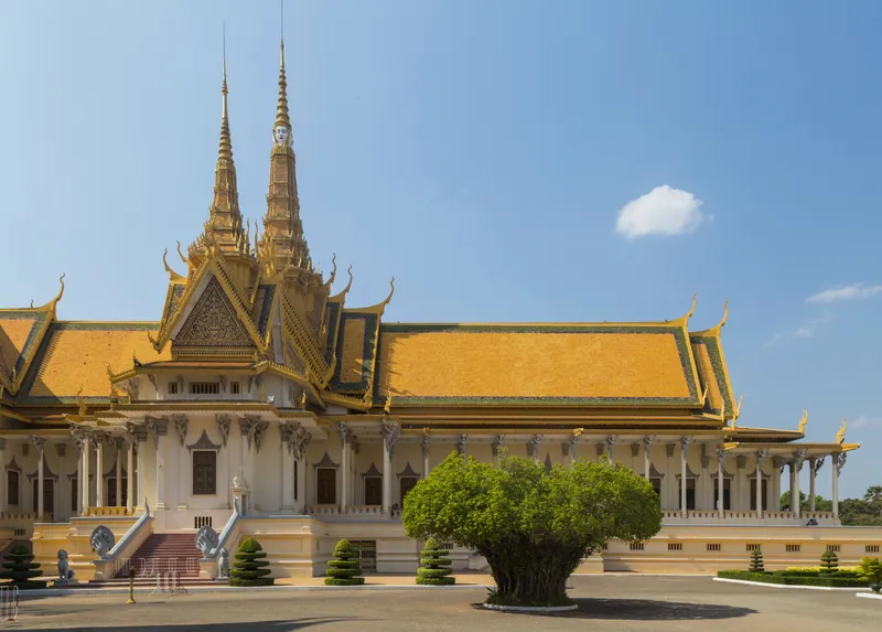 The Throne Hall of the Royal Palace in Phnom Penh, a cream building with tiered orange and green roofs and a tall gilded spire, under a clear blue sky