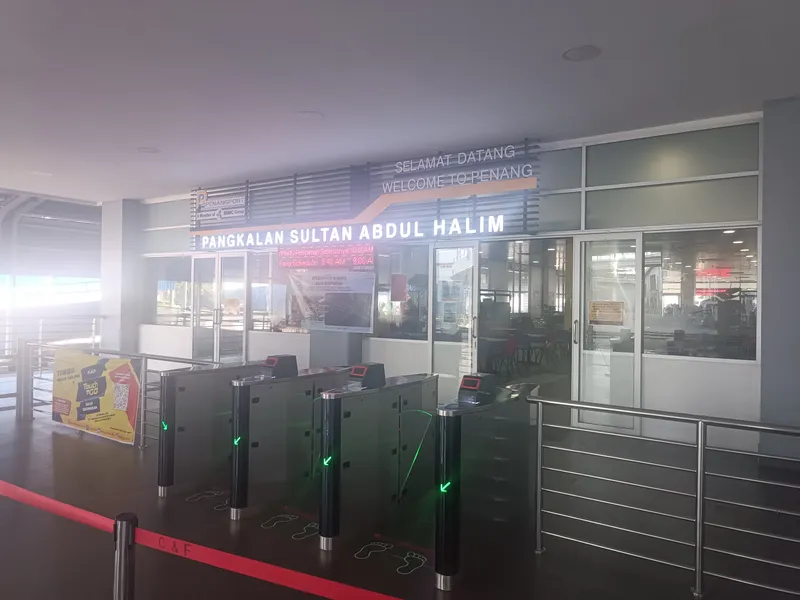 Ticket gates under a lit sign reading Pangkalan Sultan Abdul Halim and Welcome to Penang